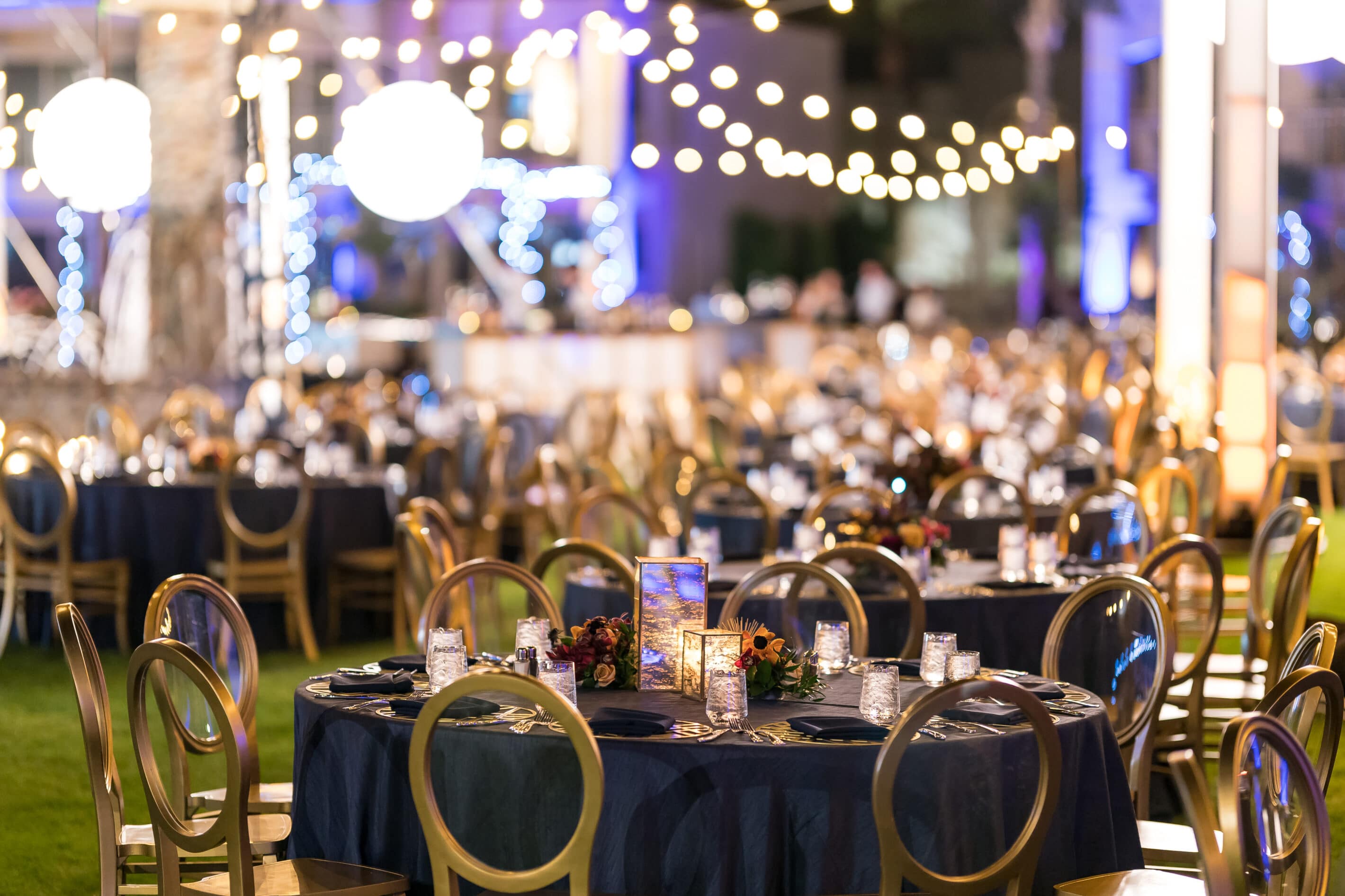 Elegant corporate dining dinner event for indoor or outdoor space at a Scottsdale resort or venue. Dining under the stars with blue and gold tones, bistro lighting and candle light.